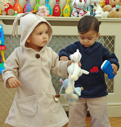 Two toddlers wearing Norvella hood jumpers playing with toys in a nursery.